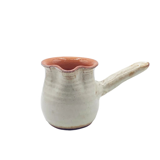 A small handmade ceramic coffee pot with a flared rim and a short handle, featuring a textured off-white glaze and a terracotta-colored interior, set against a plain light gray background.